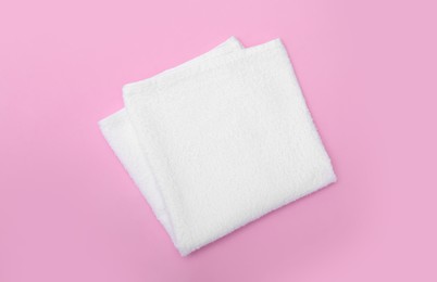 Folded white beach towel on pink background, top view