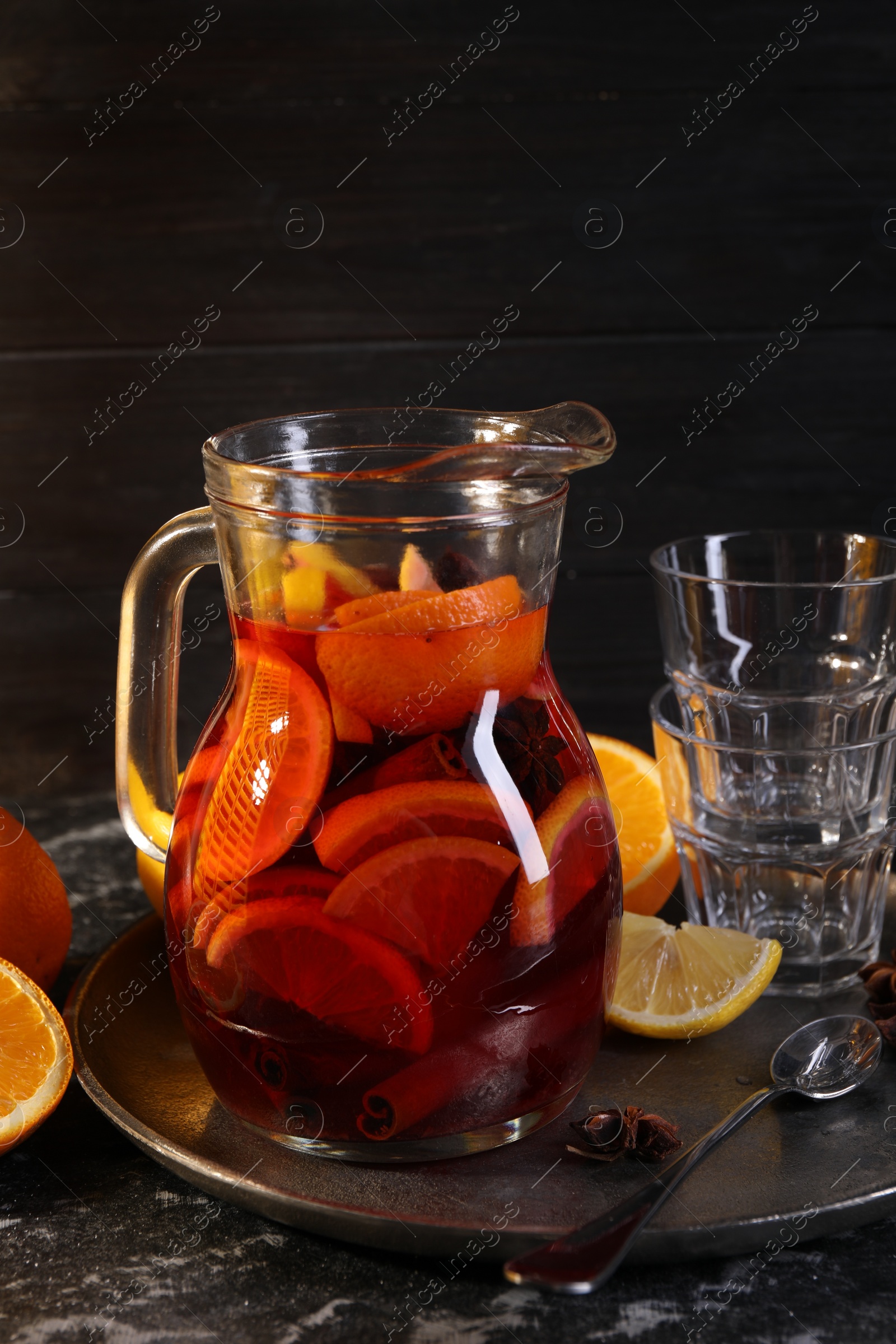 Photo of Jug of aromatic punch drink and ingredients on black table