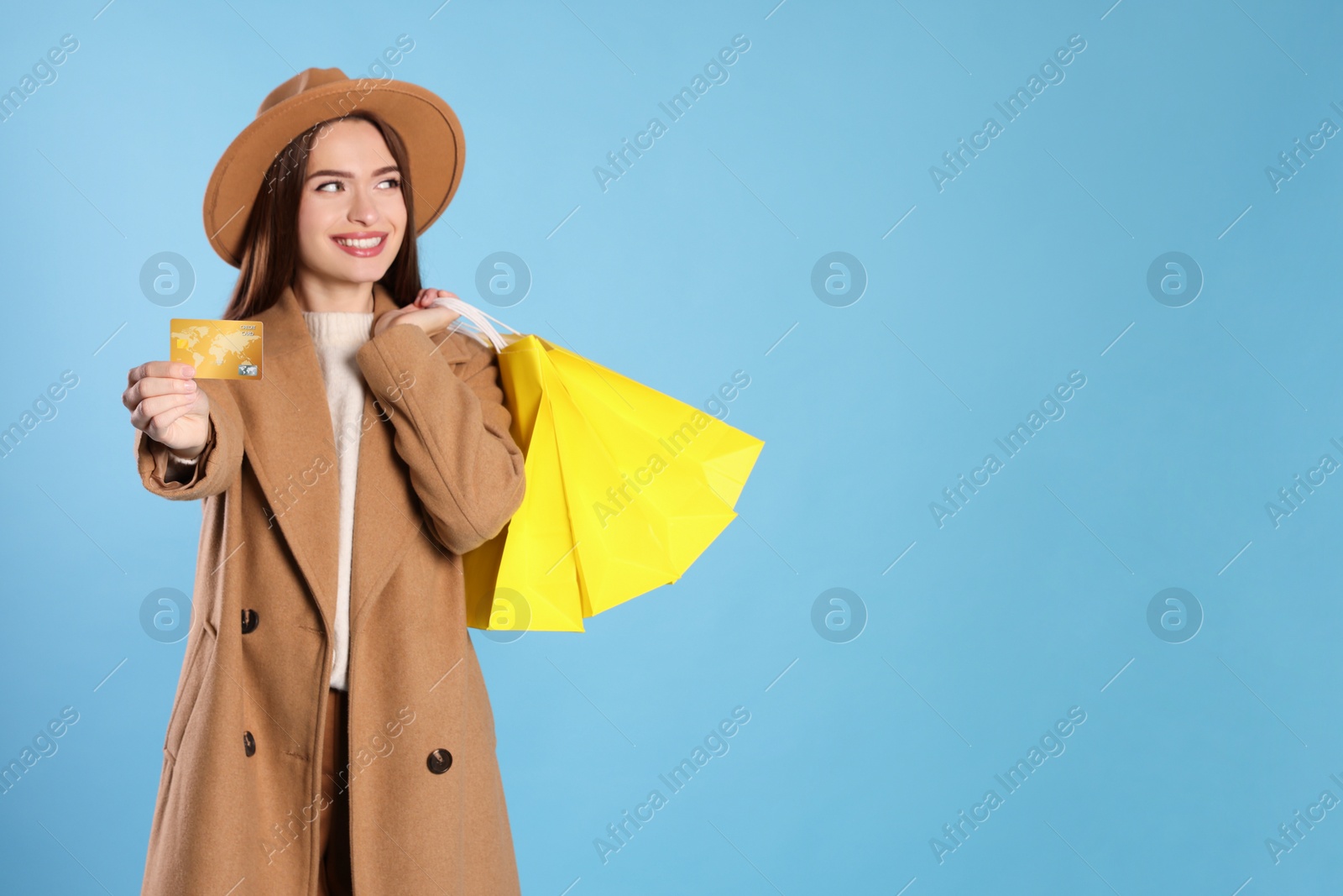 Photo of Happy young woman holding shopping bags against light blue background, focus on hand with credit card. Big sale