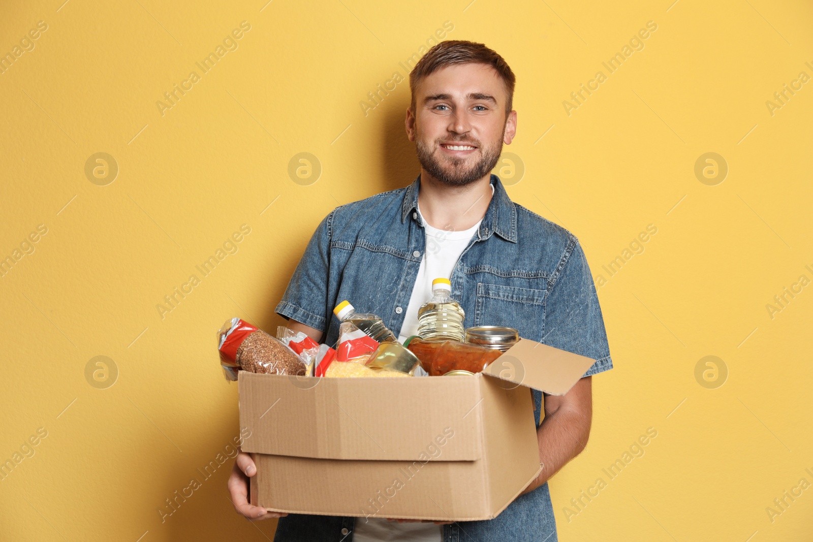 Photo of Young man holding box with donations on color background