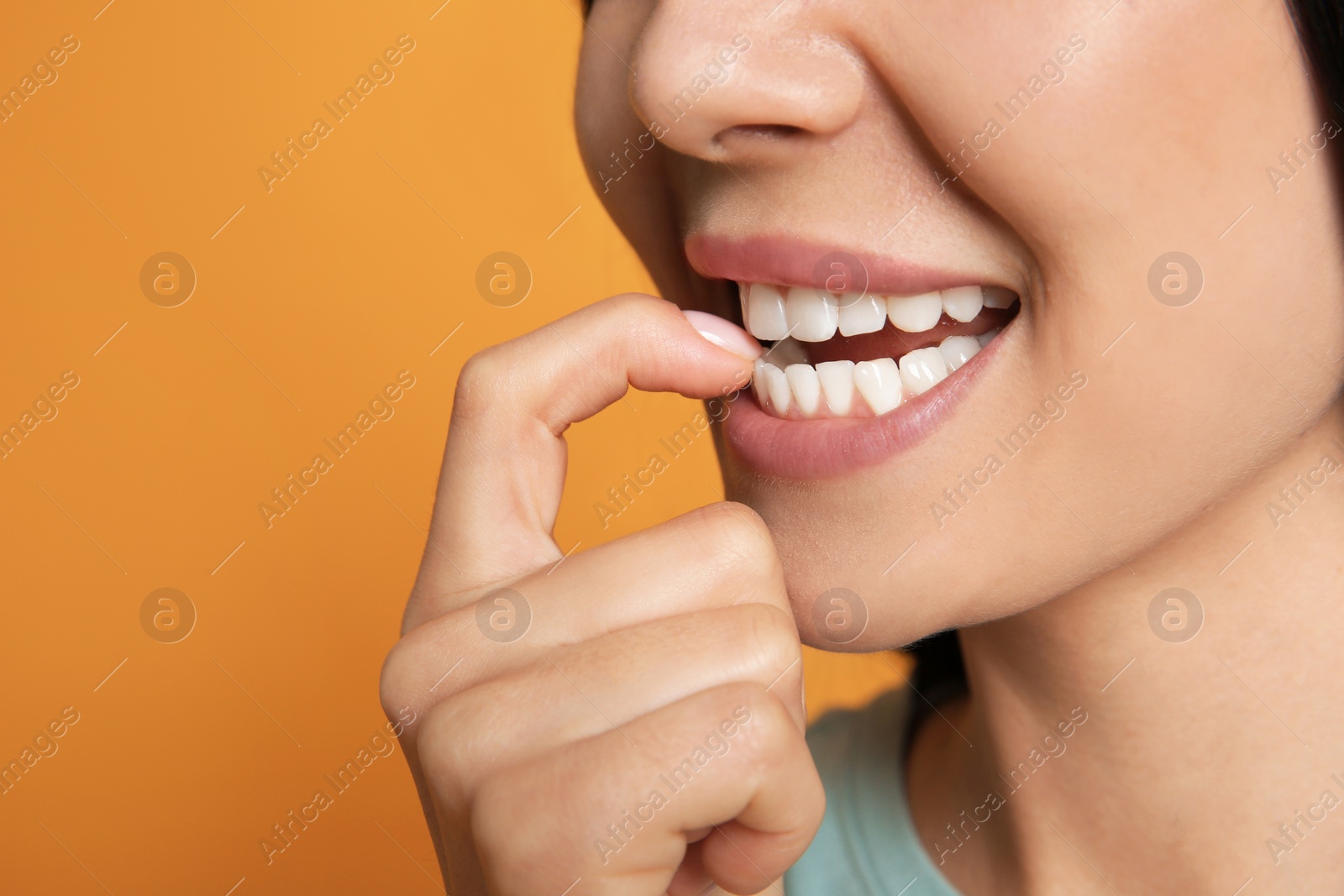 Photo of Young woman biting her nails on yellow background, closeup