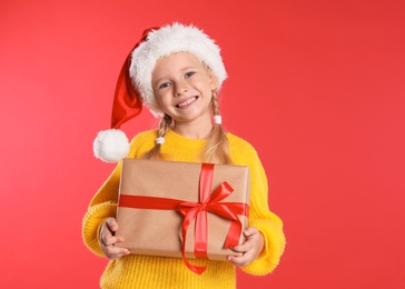 Happy little child in Santa hat with gift box on red background. Christmas celebration