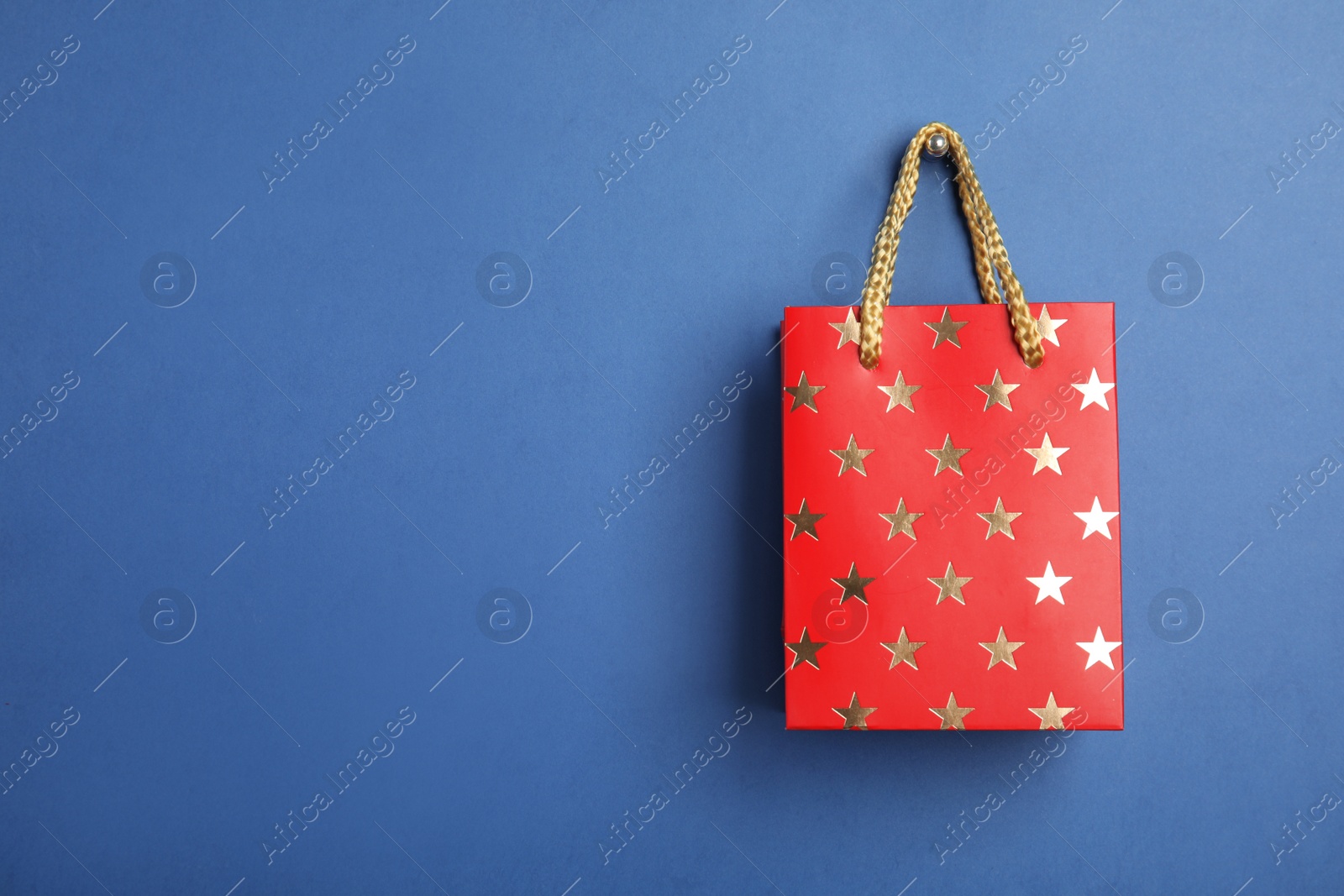 Photo of Red shopping paper bag with star pattern on blue background, space for text