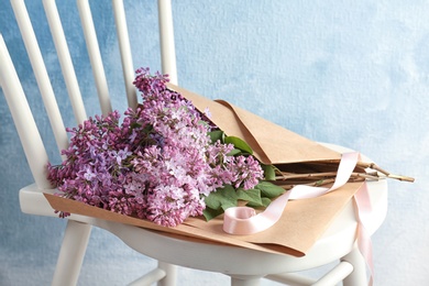 Photo of Beautiful blossoming lilac on chair against color background. Spring flowers