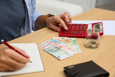 Man counting money with calculator at table indoors, closeup