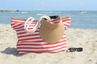 Photo of Stylish striped bag with visor cap and sunglasses on sandy beach near sea