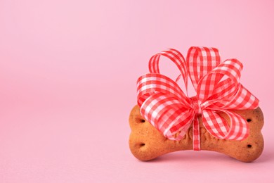 Bone shaped dog cookie with bright bow on pink background, closeup. Space for text