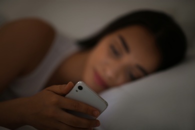 Photo of Young woman with nomophobia using smartphone in bed at night, focus on hand. Insomnia concept