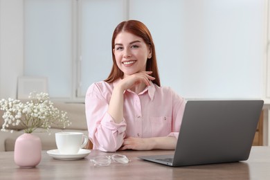 Photo of Happy woman with laptop at wooden table in room
