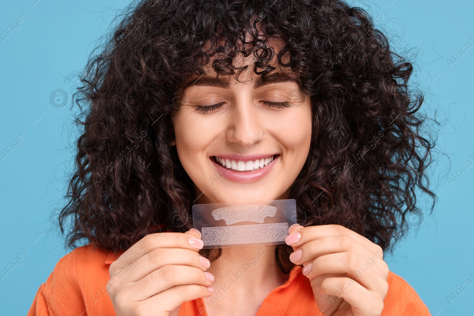 Photo of Young woman holding teeth whitening strips on light blue background