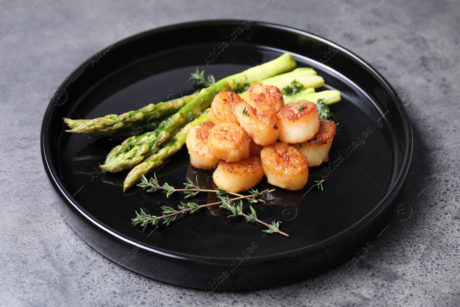 Photo of Delicious fried scallops with asparagus and thyme on grey table