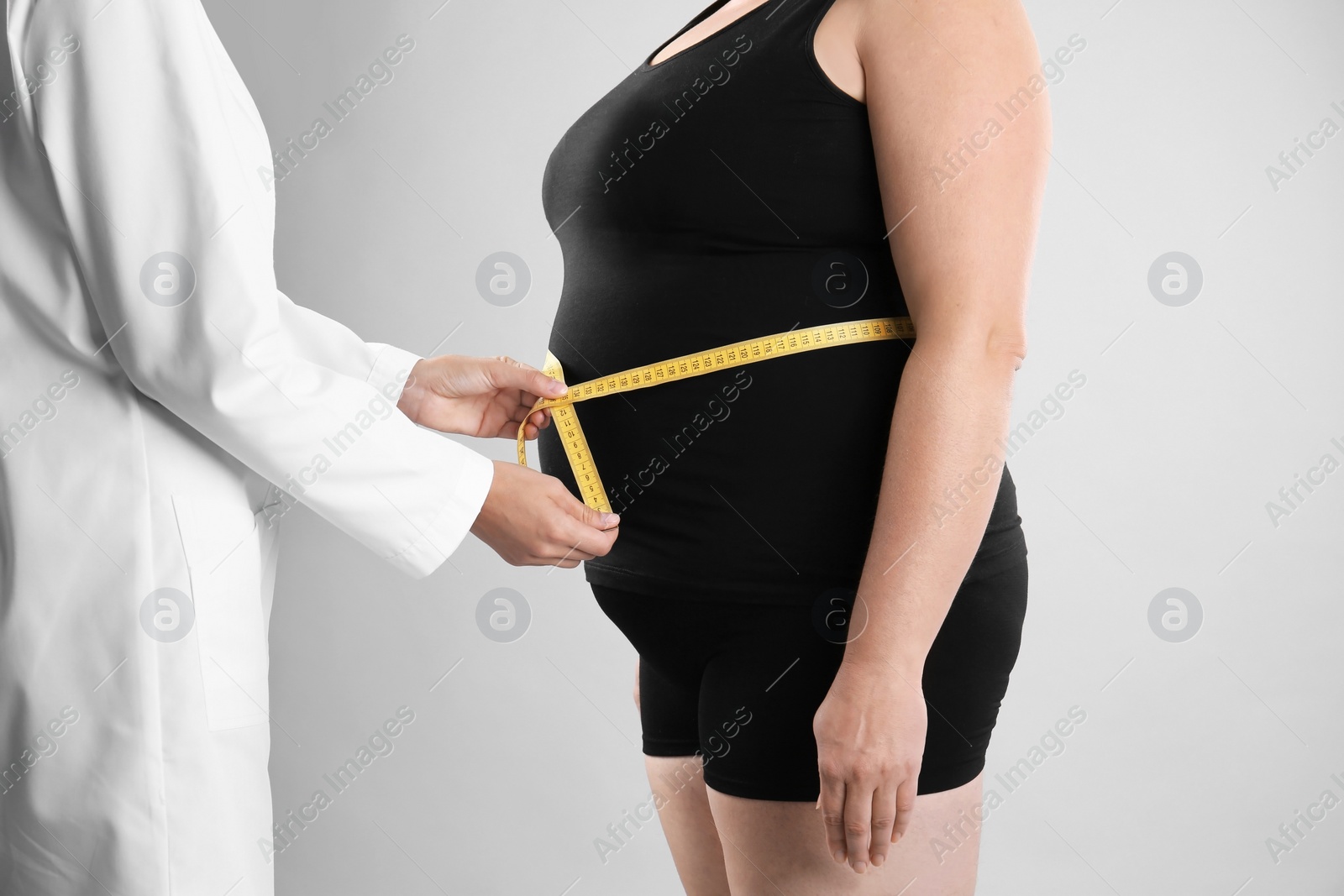 Photo of Doctor measuring fat woman's waist on grey background. Weight loss