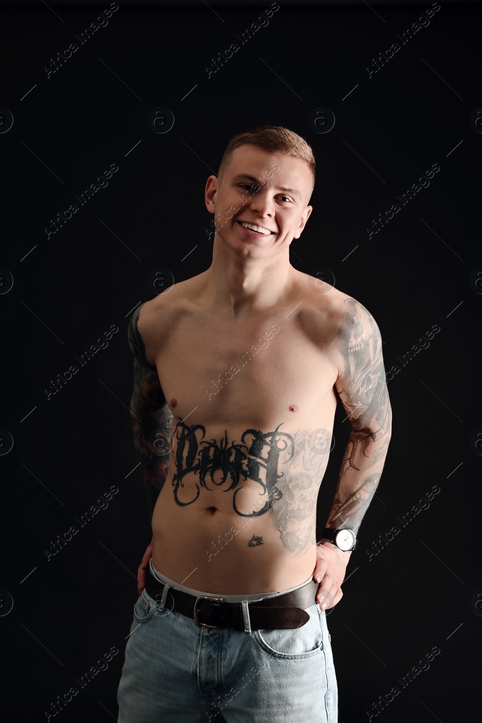 Photo of Smiling shirtless young man with tattoos on black background