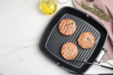 Photo of Grill pan with tasty fried hamburger patties and seasonings on white marble table, flat lay. Space for text