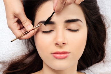 Photo of Young woman having professional eyebrow correction procedure in beauty salon, closeup