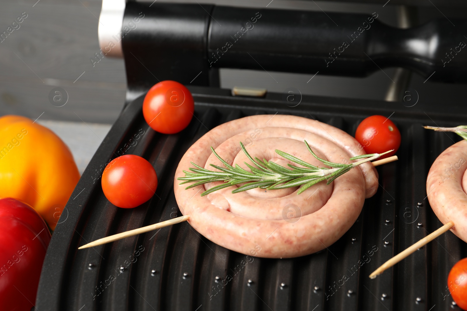 Photo of Electric grill with homemade sausage, rosemary and tomatoes on table, closeup