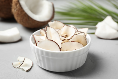 Photo of Tasty coconut chips in bowl on grey table