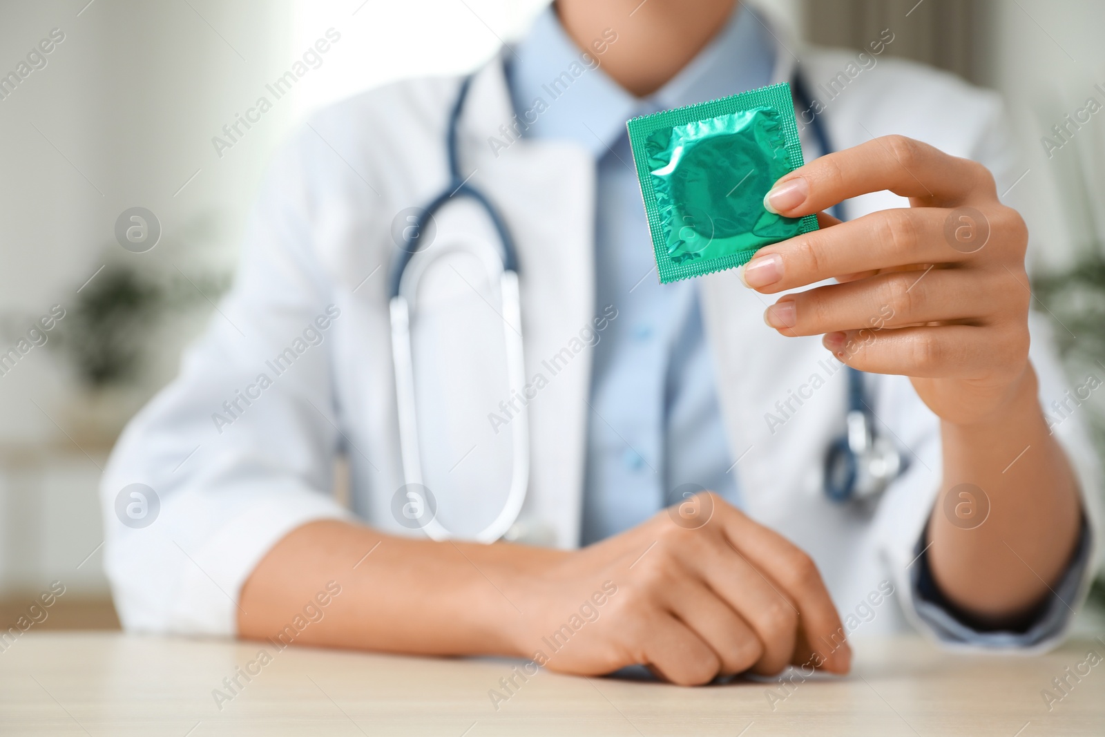 Photo of Female doctor holding condom at table indoors, closeup. Safe sex concept