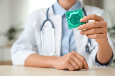 Photo of Female doctor holding condom at table indoors, closeup. Safe sex concept