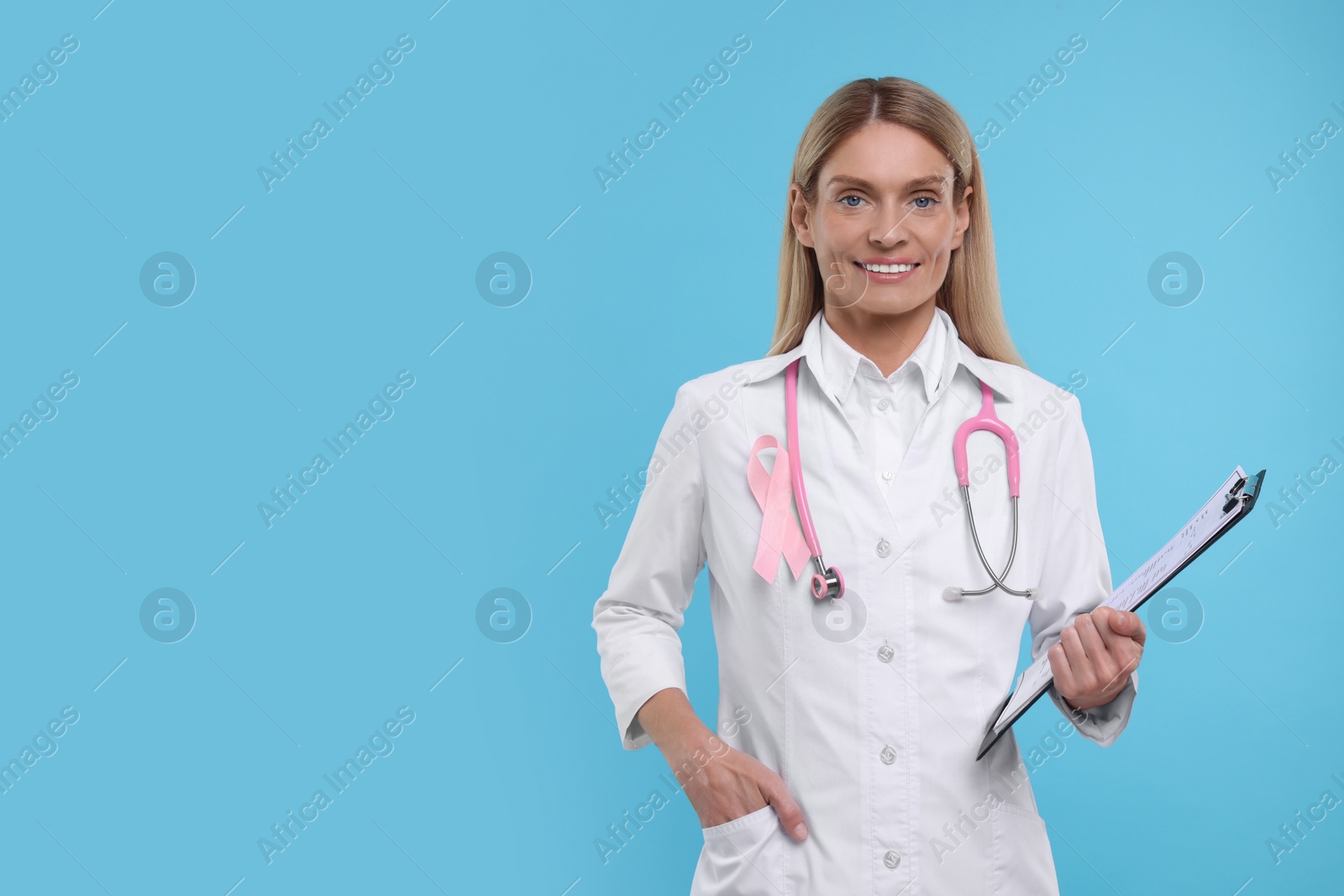 Photo of Doctor with pink ribbon, clipboard and stethoscope on light blue background, space for text. Breast cancer awareness