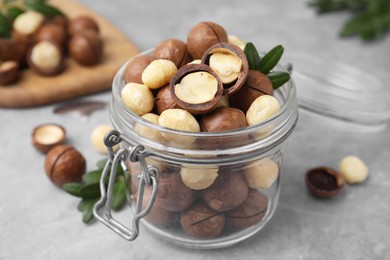 Photo of Tasty Macadamia nuts in jar on light grey table, closeup