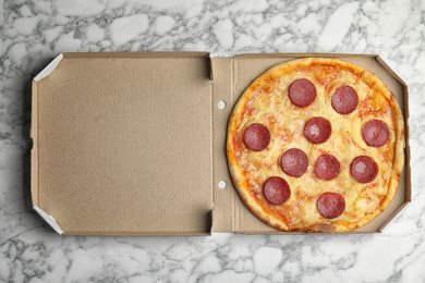 Photo of Tasty pepperoni pizza in cardboard box on white marble table, top view