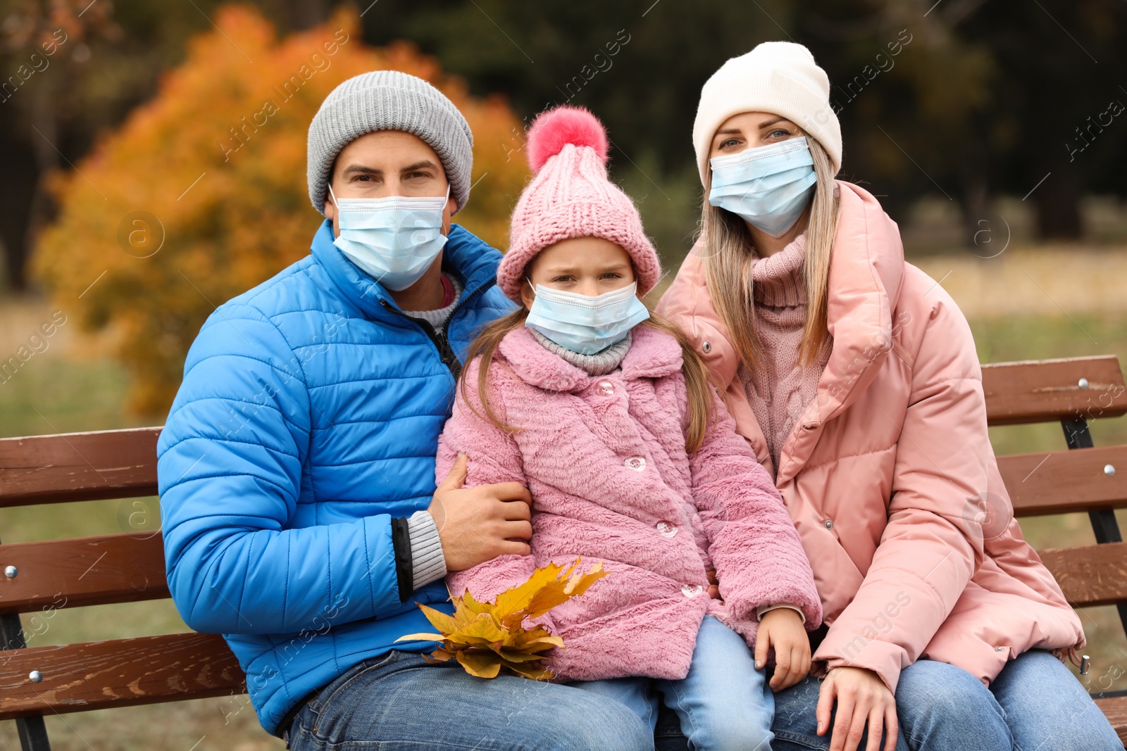 Photo of Family in medical masks spending time outdoors on autumn day. Protective measures during coronavirus quarantine