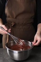 Woman with whisk mixing chocolate cream at grey table against black background, closeup