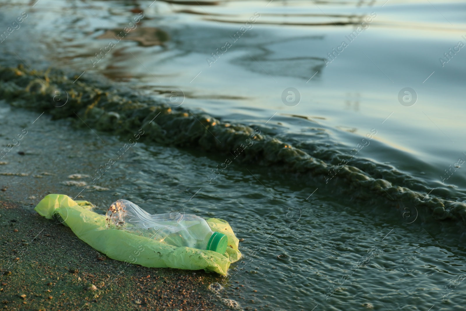 Photo of Used plastic bag and bottle near water at beach, space for text. Environment pollution