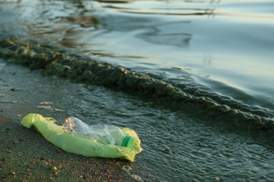 Photo of Used plastic bag and bottle near water at beach, space for text. Environment pollution