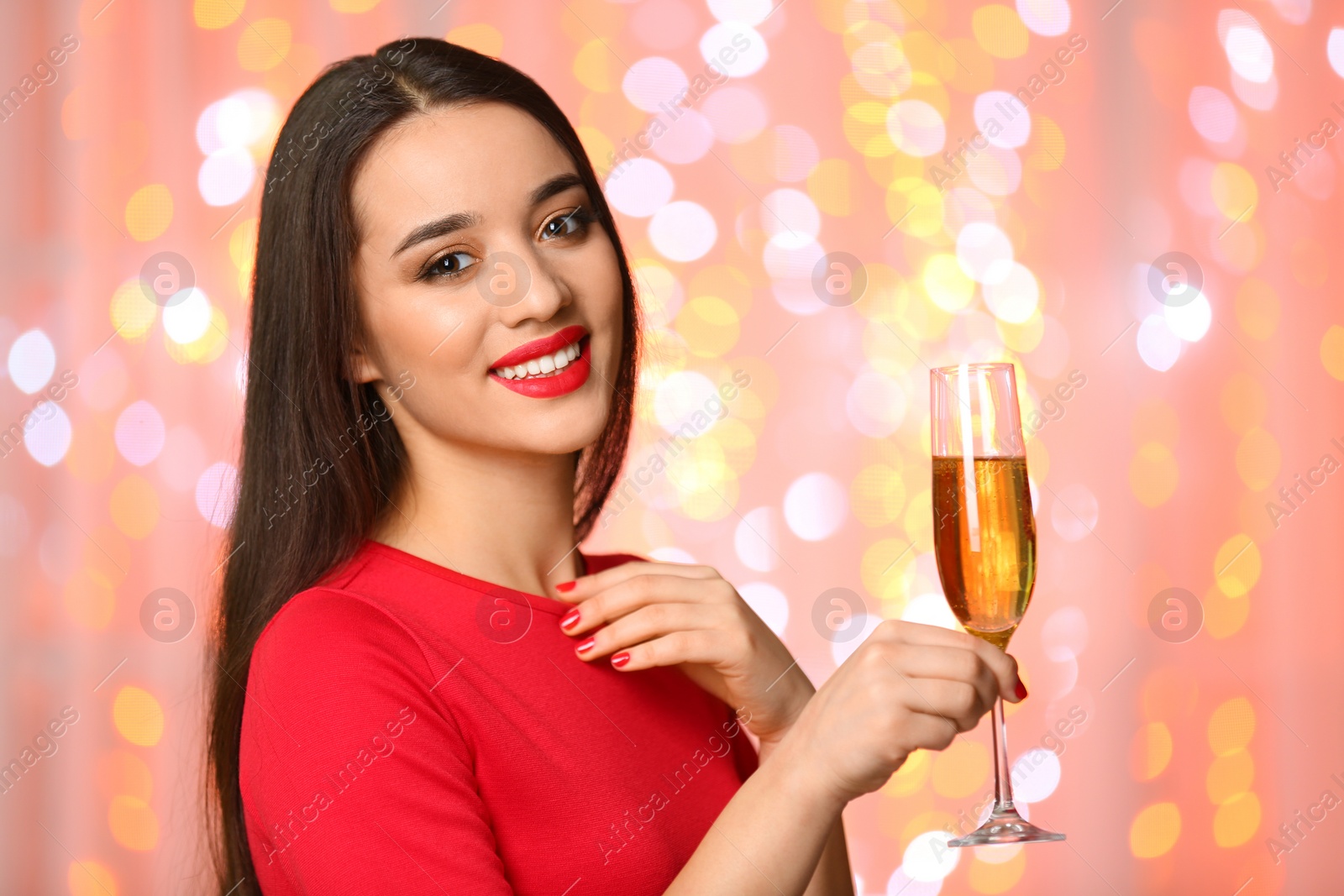 Photo of Portrait of smiling young woman with glass of champagne on blurred lights background