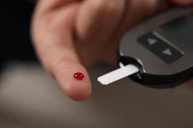 Diabetes test. Man checking blood sugar level with glucometer on blurred background, closeup