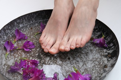 Photo of Woman soaking her feet in bowl with water and flowers, closeup. Spa treatment