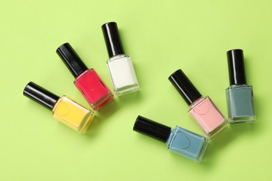 Photo of Colorful nail polishes in bottles on green background, flat lay