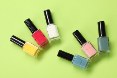 Colorful nail polishes in bottles on green background, flat lay