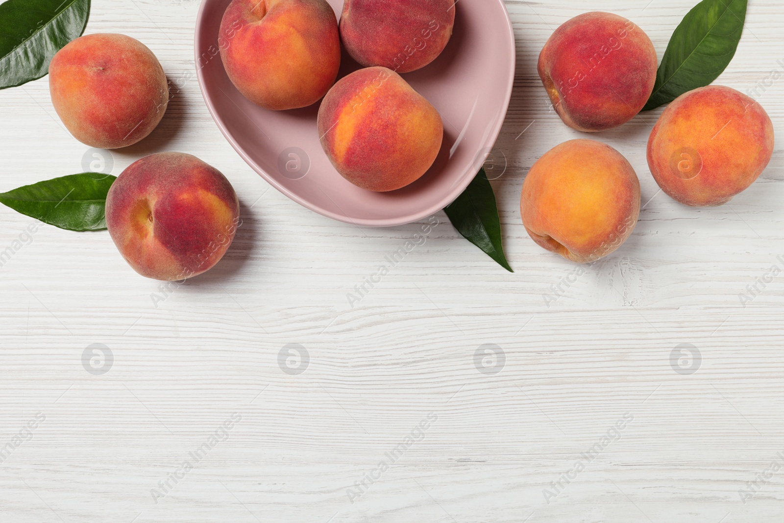 Photo of Many whole fresh ripe peaches and green leaves on white wooden table, flat lay. Space for text