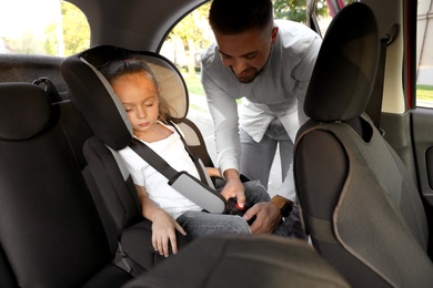 Photo of Father fastening his sleeping daughter with car safety seat belt. Family vacation