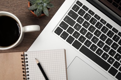 Photo of Modern laptop, notebook, pencil, cup of coffee and houseplant on wooden table, flat lay