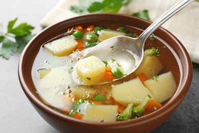 Spoon of fresh homemade vegetable soup over full bowl on grey table, closeup