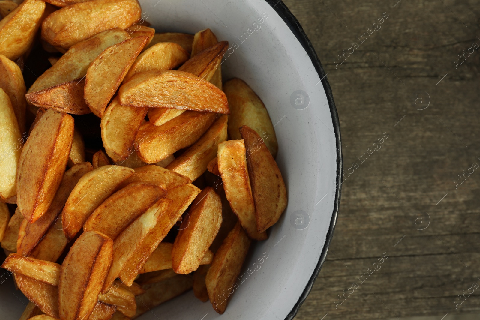 Photo of Metal bowl with delicious fried potato wedges on wooden table, top view. Space for text