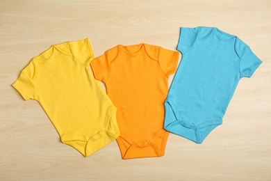 Different baby bodysuits on wooden background, top view