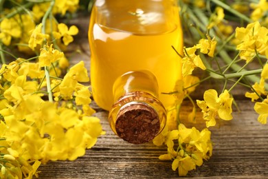Photo of Rapeseed oil in glass bottle and beautiful yellow flowers on wooden table, closeup