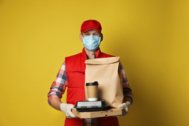 Courier in protective mask and gloves holding order on yellow background. Food delivery service during coronavirus quarantine