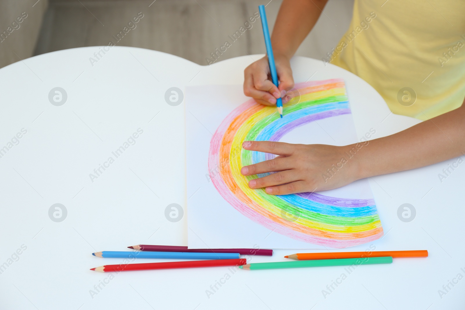 Photo of Little child drawing rainbow at white table, closeup. Stay at home concept