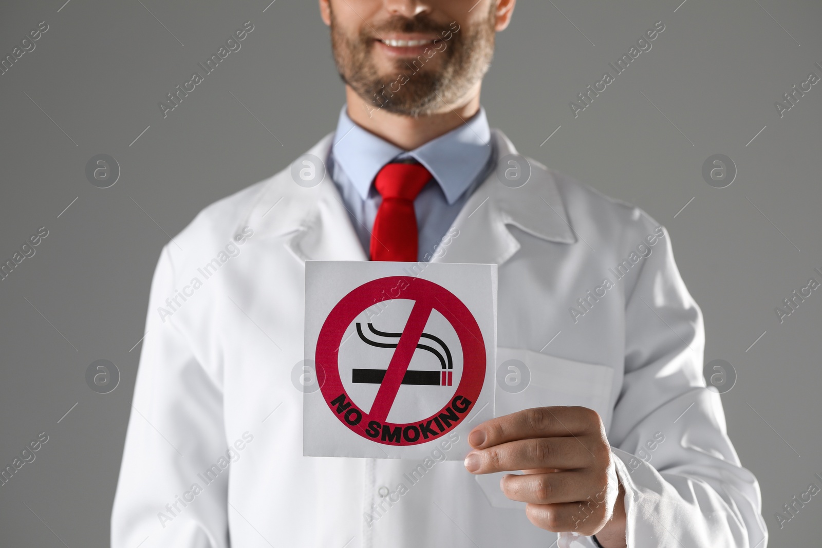 Photo of Doctor holding card with no smoking sign on gray background, closeup