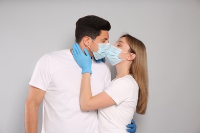 Photo of Couple in medical masks and gloves trying to kiss on light background