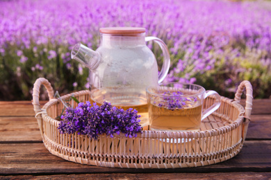 Photo of Tasty herbal tea and fresh lavender flowers in tray on wooden table outdoors, closeup