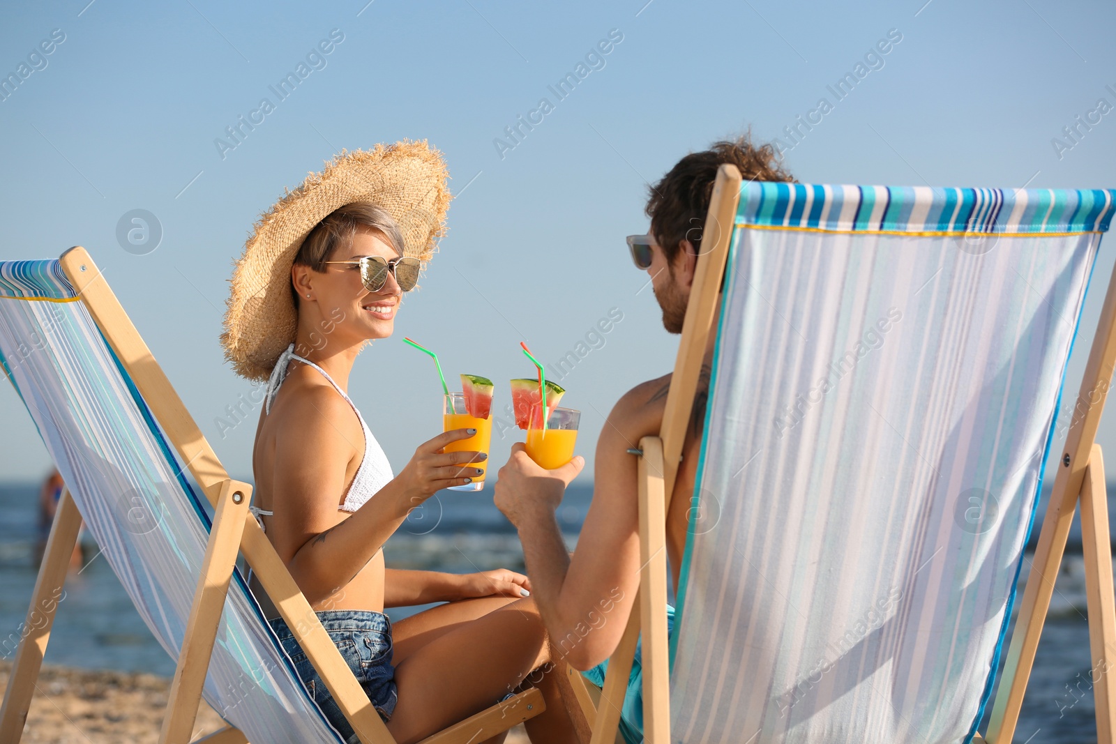 Photo of Young couple with cocktails in beach chairs at seacoast