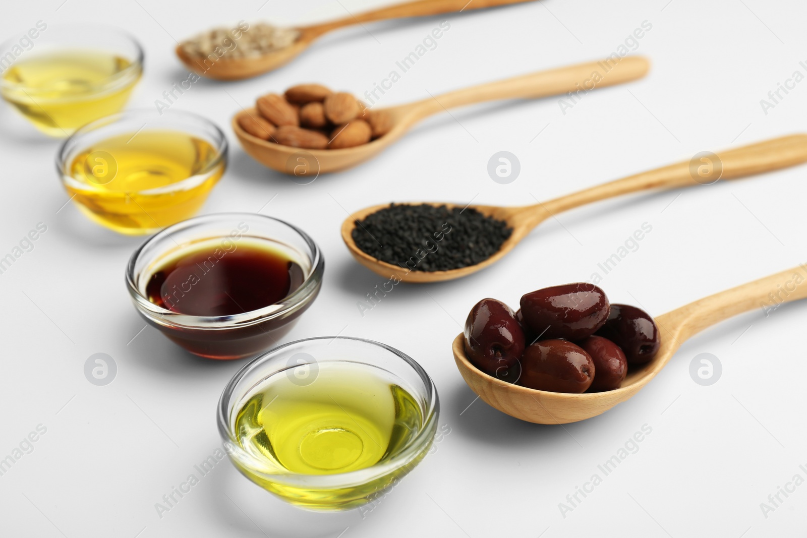 Photo of Vegetable fats. Different cooking oils in bowls and spoons with ingredients on white background