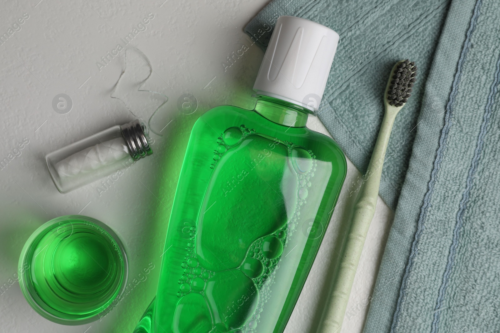 Photo of Fresh mouthwash in bottle, glass, toothbrush and dental floss on light background, flat lay